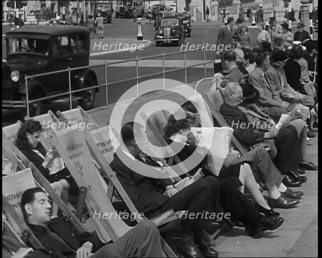 British Holidaymakers Sitting on Deckchairs on the Promenade at Brighton and Cars Driving..., 1938. Creator: British Pathe Ltd.