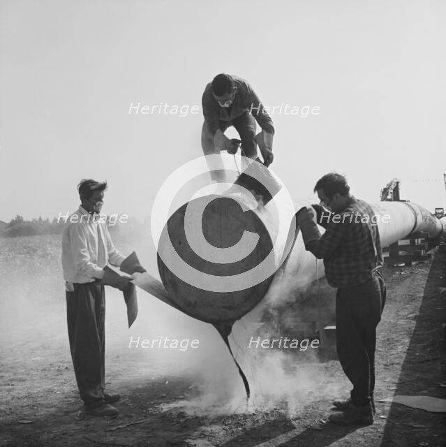 Workers wrapping and sealing the end of a steel pipe on the Fens gas pipeline, Norfolk, 24/07/1967. Creator: John Laing plc.
