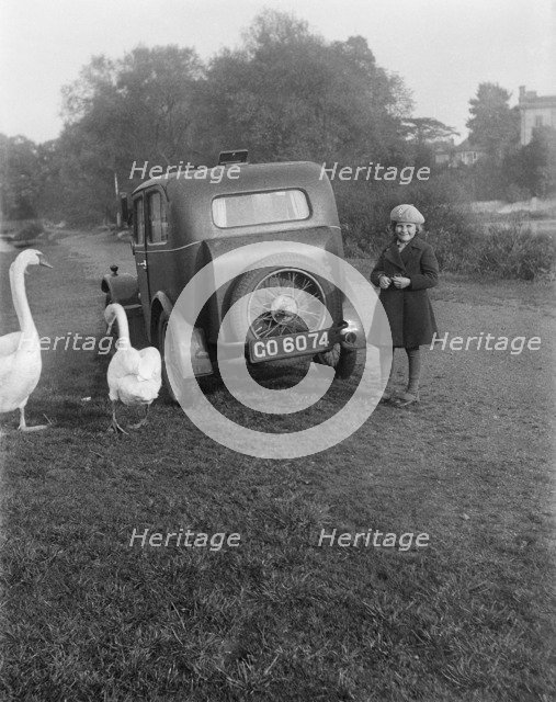 A young girl next to a motor car, probably an Austin 7, with two swans, c1930s. Artist: Unknown.