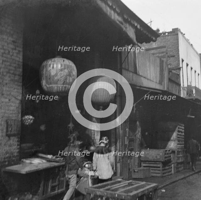 Two women and a child walking down a sidewalk betwen crates, Chinatown, San Francisco, c1896-1906. Creator: Arnold Genthe.