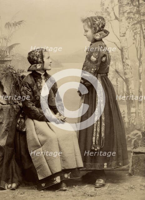 Two young girls pose in costumes from Dala-Floda with floral jackets and hats, 1890-1900. Creator: Helene Edlund.