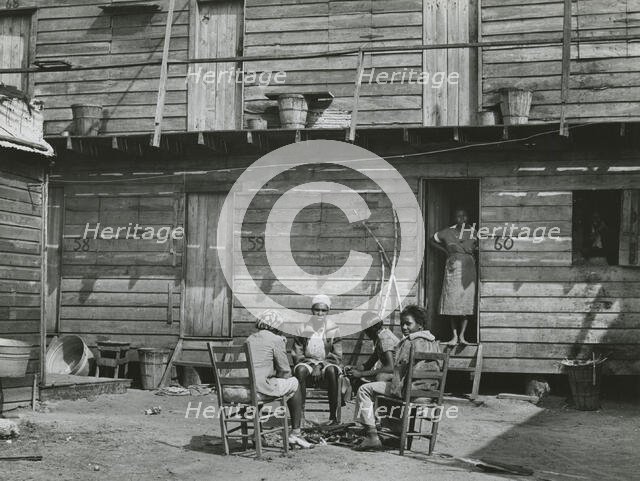 African American woman standing in doorway and African American girls sitting around..., Feb 1941. Creators: Farm Security Administration, Marion Post Wolcott.