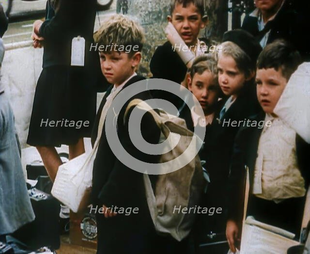 British Child Evacuees Standing on a Pavement With Bags and Boxes as Adults are Standing..., 1939. Creator: British Pathe Ltd.