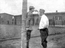 'La peine du poteau; a Zwickau: un Francais, lie au poteau, recoit d'un prisonnier roumain..., 1917. Creator: Unknown.