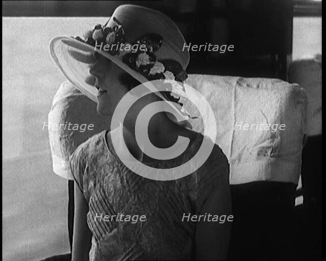Female Civilian Wearing a Large Fashionable Hat Decorated with Flowers Seating at the Window...1920. Creator: British Pathe Ltd.