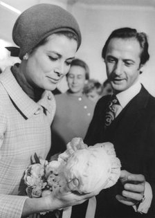 Princess Grace examines a bonnet in a Baby Dior boutique with the help of Marc Bohain. Artist: Unknown