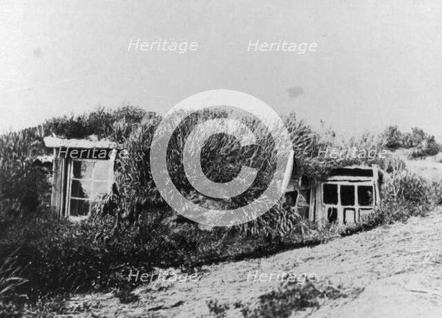 An Aleut house, which is a hole in the earth covered with a framework of driftwood..., c1900-c1930. Creator: Unknown.