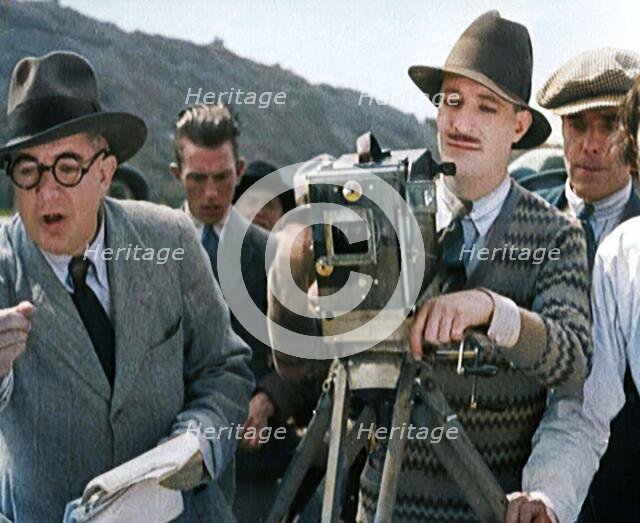 A Male Cameraman Cranking a Camera On a Film Set as the Male Director Instructs Actors, 1920s. Creator: British Pathe Ltd.