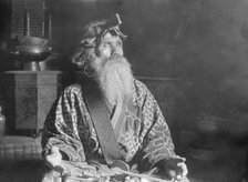 Ainu chief wearing a headdress seated with a sword in his lap, 1908. Creator: Arnold Genthe.