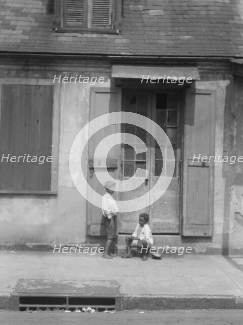 Two children outside a door with shutters in the French Quarter, New Orleans, between 1920 and 1926. Creator: Arnold Genthe.