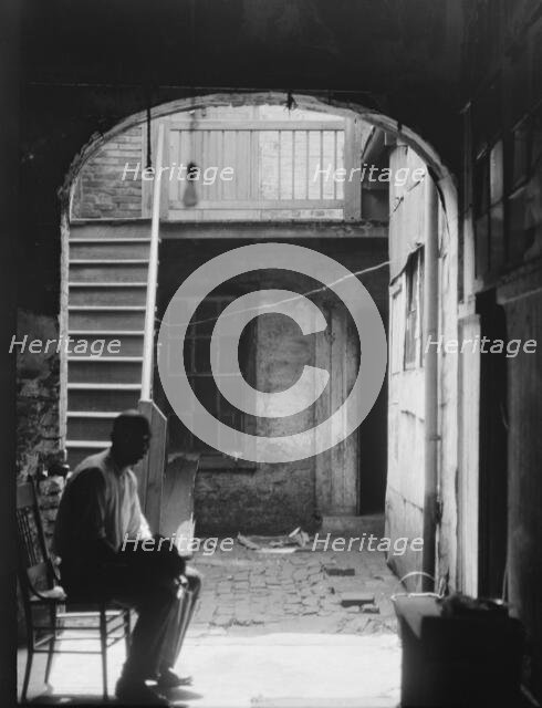 Man seated in archway leading to a courtyard, New Orleans, between 1920 and 1926. Creator: Arnold Genthe.
