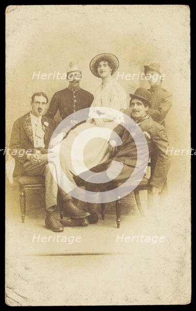 Amateur actors sitting down, surrounding a man in drag seated in the centre, [1910-1919?]. Creator: Unknown.