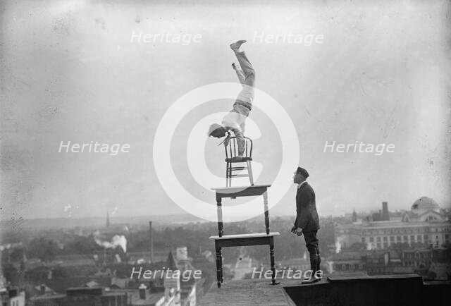 J. Reynolds, Performing Acrobatic And Balancing Acts On High Cornice Above 9th Street, N.W., 1917. Creator: Harris & Ewing.