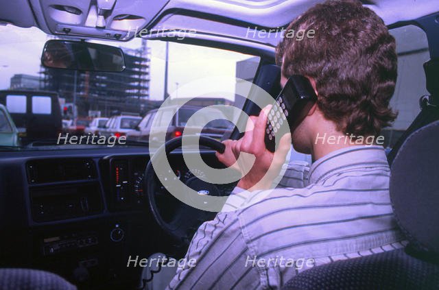 Man driving whilst using built-in car telephone 1990. Creator: Unknown.