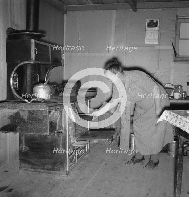 Mrs. Wardlow baking corn bread in her dugout basement home, Dead Ox Flat, Oregon, 1939. Creator: Dorothea Lange.
