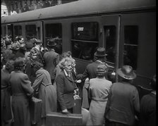 Male and Female Passengers, Some Holding Suitcases, on a Platform of a Large Train Station..., 1938. Creator: British Pathe Ltd.