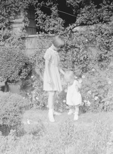 Children of Mrs. George Eustis standing outdoors in a garden, between 1911 and 1942. Creator: Arnold Genthe.