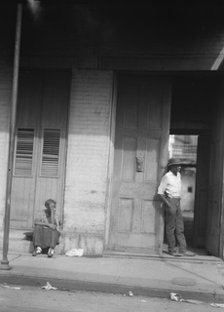Woman sitting on steps and man standing in a doorway, New Orleans, between 1920 and 1926. Creator: Arnold Genthe.