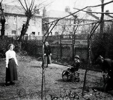 A physically disabled boy sitting in a wheelchair in the back garden of a semi..., c1910/1925. Creator: Unknown.