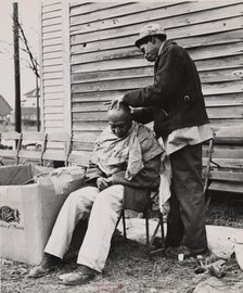 Negro getting a haircut in front of church which houses flood refugees. Sikeston, Missouri, 1937-02. Creators: Farm Security Administration, Russell Lee.