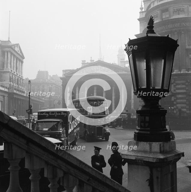 View past a lamp showing the busy traffic outside The Bank of England..., London, probably 1960s. Creator: John Gay.