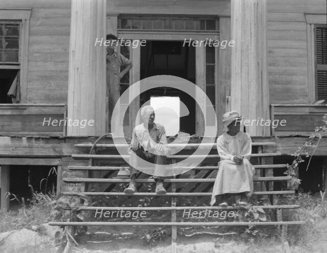 Ex-slave and wife on steps of plantation house now in decay, Greene County, Georgia, 1937. Creator: Dorothea Lange.