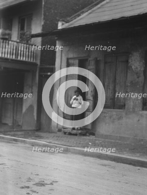 View from across street of a woman standing in a doorway in the French Quarter, New..., c1920-c1926. Creator: Arnold Genthe.