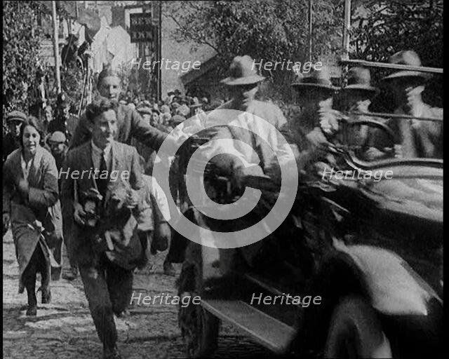 Crowd Chasing a Motorcar as It Climbs up a Hilly Cobbled Street, 1920. Creator: British Pathe Ltd.