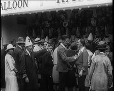 A Crowd of People Standing in Front of a Carnival Game. A Man in a Clown's Hat Encourages..., 1924. Creator: British Pathe Ltd.