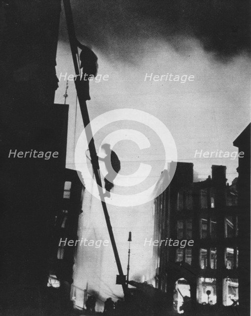 'Out in the Blitz, silhouetted aganinst the light of fires, rescue men climb into a building in St.  Artist: Unknown.