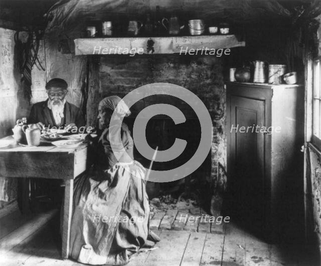 Old African American couple eating at the table by fireplace, rural Virginia, 1899 or 1900. Creator: Frances Benjamin Johnston.