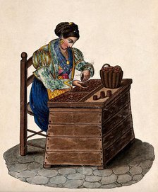 A woman sits at a wooden box counting money out of a basket onto a tray. Creator: Unknown.