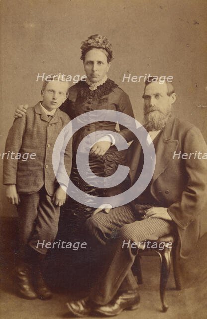 Portrait of an unidentified family: mother and son standing, bearded father seated, 1865-1875. Creator: John McKean.