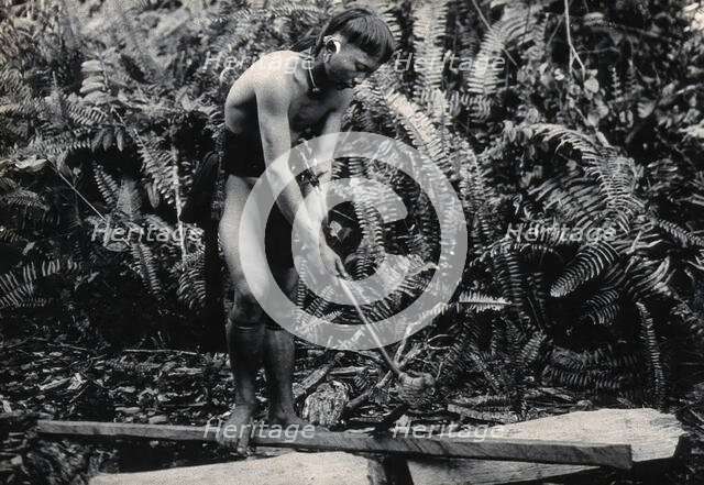 Sarawak: a Kenyah worker cutting a blowpipe from a block of wood, c1900. Creator: Unknown.