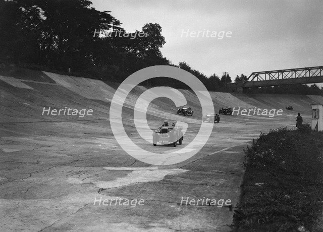 Cars racing on the Members Banking at a JCC Members Day, Brooklands. Artist: Bill Brunell.