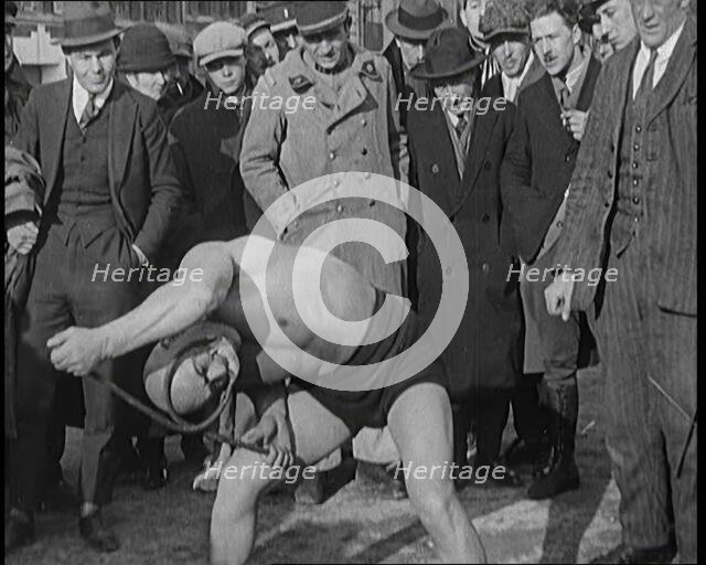 A Strongman Bending an Iron Bar Around His Head, 1921. Creator: British Pathe Ltd.