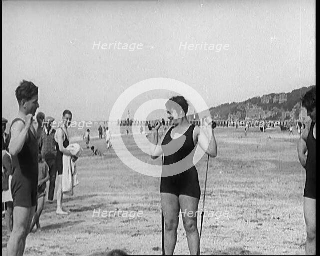 Female Civilian Wearing a Swimsuit Exercising with Elastic Bands on a Beach, 1920. Creator: British Pathe Ltd.