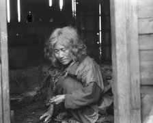 Ainu woman seated in the doorway of a wooden hut, 1908. Creator: Arnold Genthe.