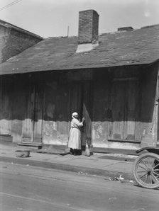 View from across street of a woman with a broom standing in a doorway, New Orleans, c1920-c1926. Creator: Arnold Genthe.