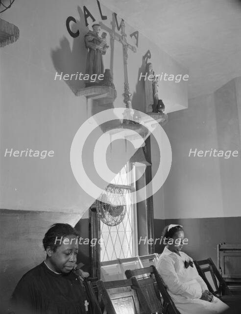 Sitting beneath the emblem of the crucifixion of Jesus on Calvary, Washington, D.C., 1942. Creator: Gordon Parks.