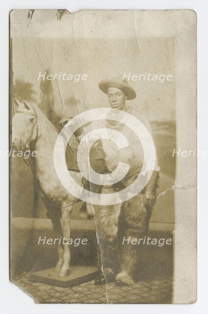 Postcard of a man posing in a Western scene in a photography studio, early 20th century. Creator: Unknown.