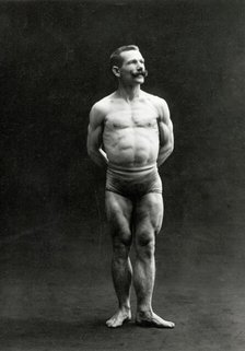 A male bodybuilder wearing bathing trunks, posing in a studio setting, between 1899 and 1908. Creator: Unknown.