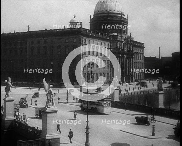 Bus Driving Down a Wide Road with a Large Building in the Background, 1933. Creator: British Pathe Ltd.