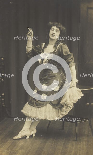 A performer in drag, wearing a large flowery dress, poses with a cigarette on stage, c1908-1910. Creator: Unknown.