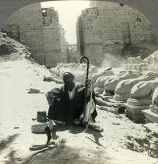 'An Egyptian Snake Charmer Piles His Trade Beside the Avenue of Sphinxes, Temple of Karnak, Thebes,  Creator: Unknown.