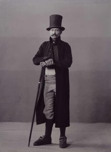 A man poses in folk costume with a long coat and a top hat, 1880-1907. Creator: Helene Edlund.