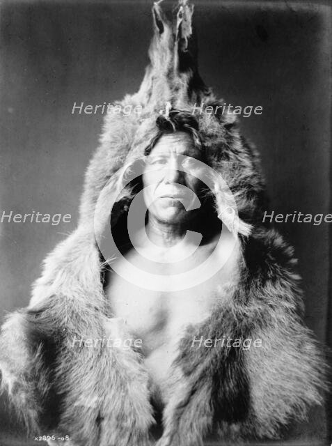 Bear's Belly, Arikara Indian half-length portrait, facing front, wearing bearskin, c1908. Creator: Edward Sheriff Curtis.