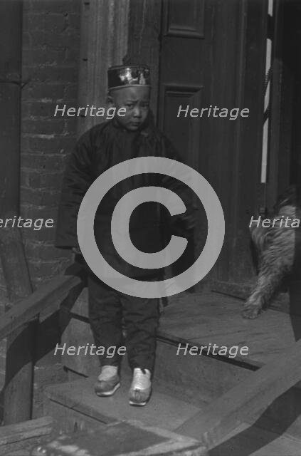 Boy standing on steps in front of a doorway, Chinatown, San Francisco, between 1896 and 1906. Creator: Arnold Genthe.
