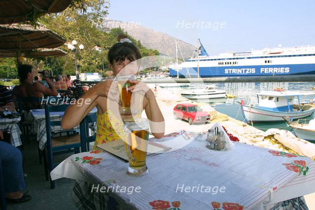 Woman enjoying a drink in a harbourside taverna, Poros, Kefalonia, Greece