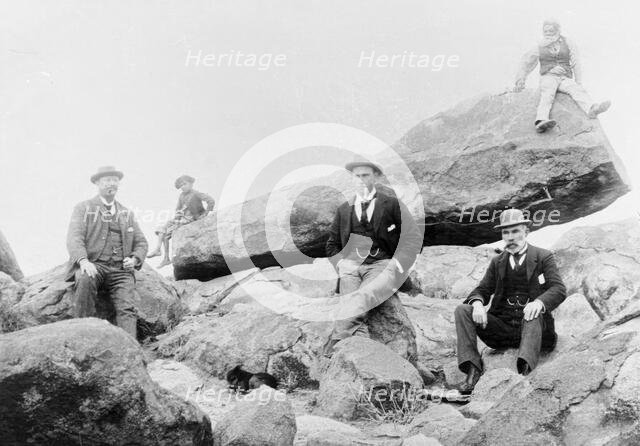 Unknown men and boy, unknown location posing on large rocks, c1900s. Creator: Robert Augustus Henry L'Estrange.